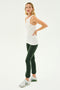 A woman in a SPLITS59 Kiki Rib Tank Full Length - White, dark green leggings, and white sneakers stands against a plain background. She has one hand on her hip and her head tilted slightly, exuding the confidence of someone who enjoys running.