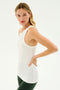 A woman with long blonde hair wearing the Kiki Rib Tank Full Length in white from SPLITS59 and dark green leggings, perfect for gym workouts or yoga, stands against a plain white background.