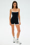 A person dressed in the SPLITS59 Monah Rigor Jumpsuit in black/white, paired with white socks and silver sneakers, stands against a plain white background.