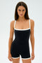 Someone stands facing forward against a plain background wearing the black and white Monah Rigor Jumpsuit by SPLITS59, featuring a fitted and sleeveless design.