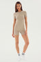 A woman with long hair is standing against a plain background, wearing a light beige Theo Rib Short - Latte by SPLITS59 and matching fitted T-shirt, embodying tailored comfort. She completes the classic design with white socks and looks directly at the camera.