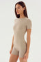A person with long hair stands wearing the fitted SPLITS59 Louise Rib Short Sleeve in Latte, paired with matching shorts made from soft modal fabric, against a plain white background.
