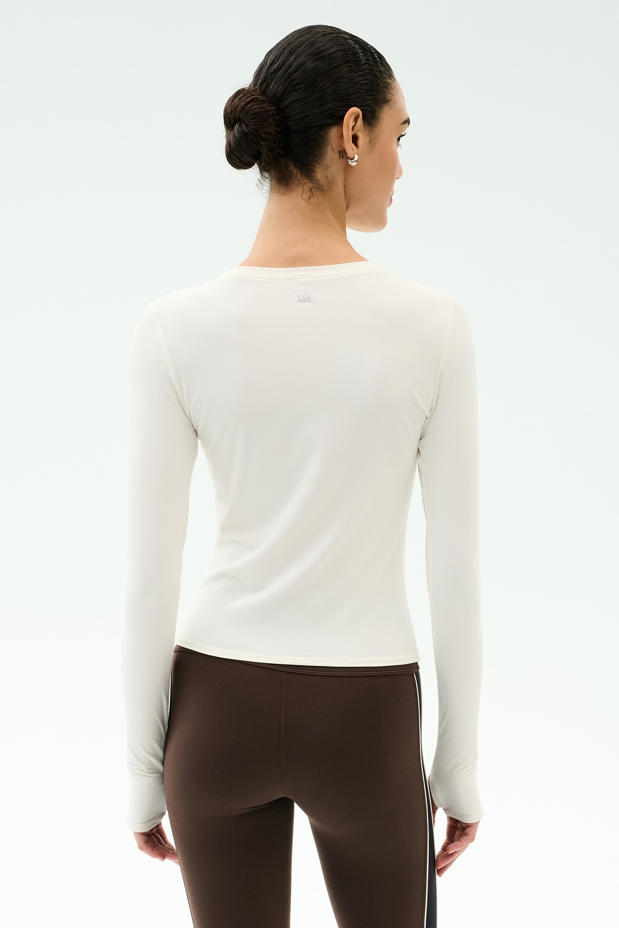 A woman with dark hair in a bun is seen from behind, wearing the SPLITS59 Airweight Lite Long Sleeve Waist Length in White—an ideal lightweight workout top for gym sessions.