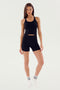 A person in a black, **SPLITS59 Ashby Rib Crop - Black** and black shorts stands on a white background. They are also wearing white socks with two black stripes, perfect attire for gym workouts.