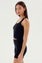 A person with long brown hair wearing the Ashby Rib Crop - Black from SPLITS59 and black shorts, made from baby rib fabric, stands facing slightly to the side against a plain white background. This outfit is perfect for intense gym workouts or casual outings.
