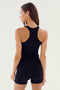 A person with long hair is wearing a black Ashby Rib Crop - Black by SPLITS59 and black shorts, facing partially away from the camera.