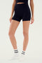 A person wearing black SPLITS59 Theo Rib Short - Black and a black sleeveless top, complemented by white socks with black stripes and white shoes, stands against a white background. Embracing tailored comfort and classic design, the person's head and feet are not visible.