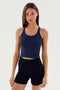 A person with long hair wearing a dark blue sleeveless Ashby Rib Crop - Indigo by SPLITS59 and black shorts stands against a plain background.