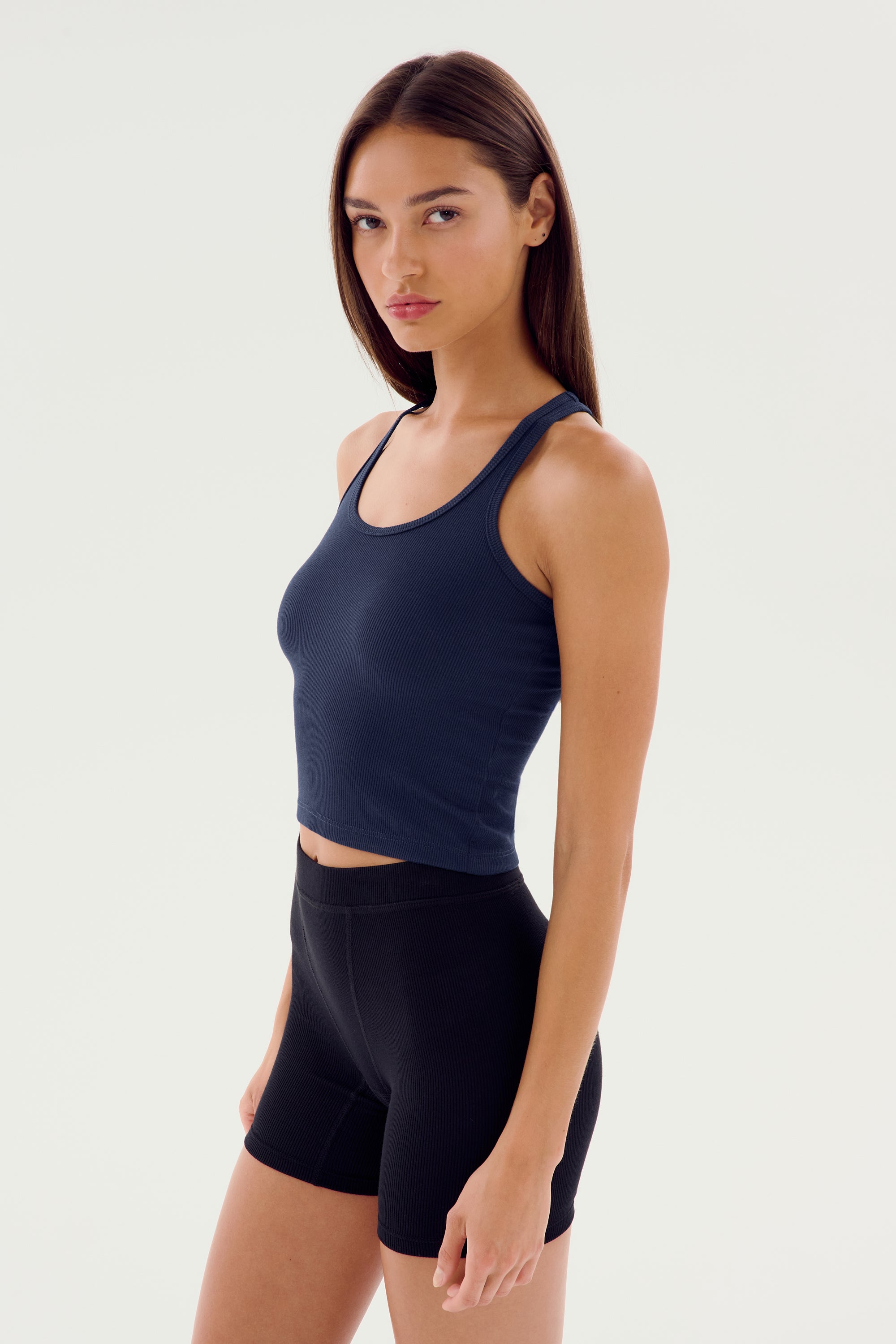 A person with long hair is wearing a navy SPLITS59 Ashby Rib Crop - Indigo and black shorts, standing against a plain white background.