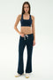 A woman stands against a plain background wearing the SPLITS59 Blaire Rib Pant in Indigo, a navy spandex sports bra, and white sneakers.