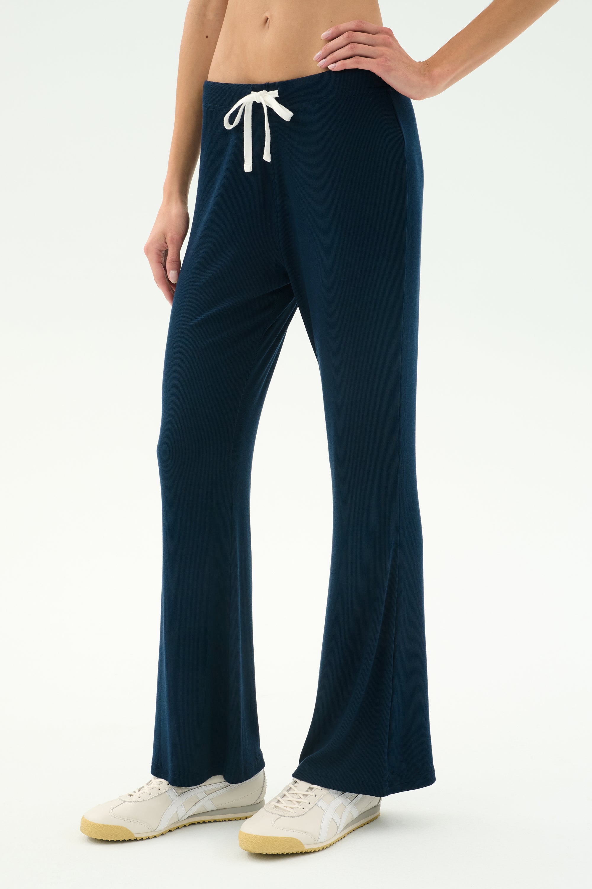 A person wears SPLITS59's Blaire Rib Pant in Indigo, made from soft modal fabric, with white sneakers—pictured waist down against a plain light backdrop.