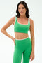 A woman models the SPLITS59 Cait Rigor Bra in Grass/White, paired with matching high-waisted leggings featuring white trim—ideal for high-impact workouts—against a plain light background.