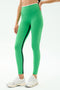 A person wearing SPLITS59 Easton Rigor High Waist 7/8 leggings in Grass/White, featuring a bright green compressive fabric with a black side stripe, paired with white athletic shoes and standing against a plain light background.