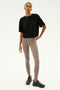 A person in a black shirt, Sprint High Waist Rigor 7/8 in Lentil by SPLITS59, and black shoes stands against a plain background.