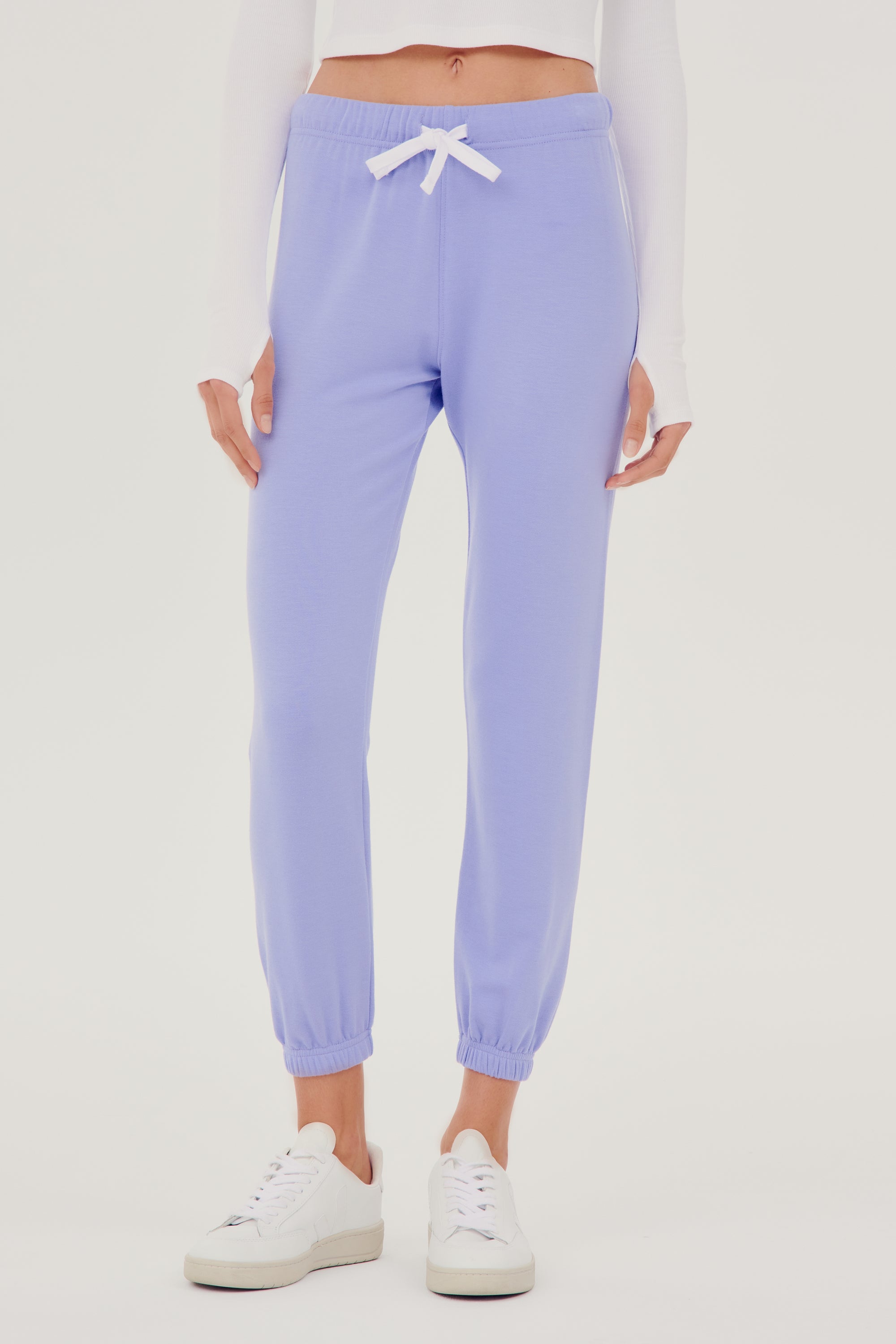 Front view of woman with straight dark brown hair wearing light purple sweatpant jogger with white drawstring and white cropped turtleneck long sleeve paired with white shoes 