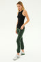 A woman with blonde hair, wearing the SPLITS59 Kiki Rib Tank Full Length in black, green pants, and white sneakers, stands against a plain background. Her toned physique hints at her dedication to CrossFit.