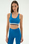 A woman wears the SPLITS59 Maci Airweight Bra in Stone Blue/Graphite with matching high-waisted leggings, standing against a plain light background.