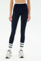A person wearing SPLITS59 Sam High Waist Rigor 7/8 navy blue leggings with white side stripes, paired with white socks featuring black stripes and gray athletic shoes, stands against a plain white background.
