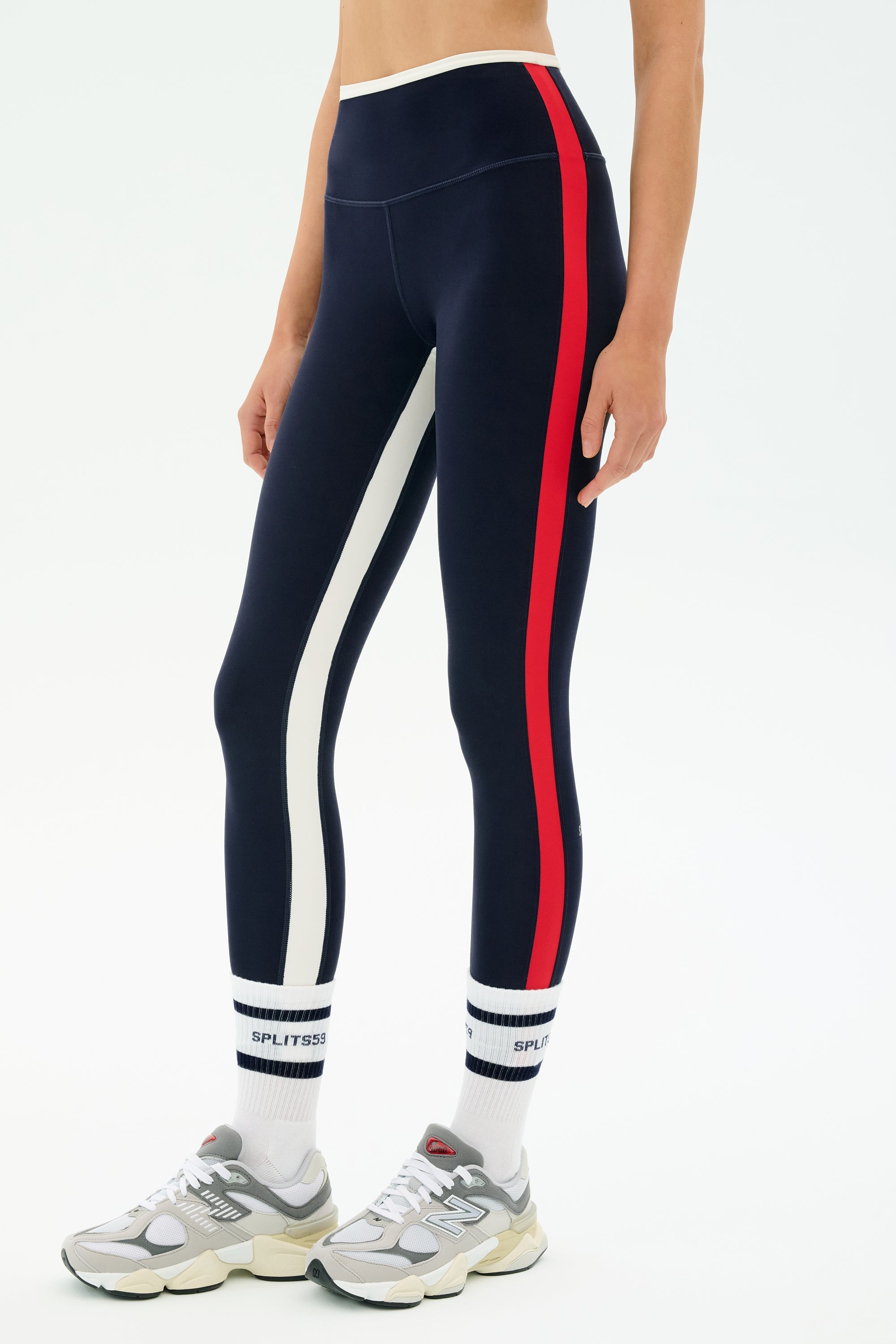 A person wearing SPLITS59 Sam High Waist Rigor 7/8 leggings in Indigo/White, white logo socks, and gray sneakers is shown from midriff to feet against a white background.