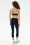 A woman with curly hair is seen from behind in a SPLITS59 Eva Rigor Double Strap Bra - Indigo/White, looking comfortable and confident for gym workouts against a plain white background.