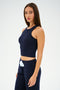 Wearing the Kiki Rib Crop Tank in Indigo by SPLITS59 and matching pants, a person stands against a plain background, looking forward.
