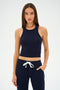 A person wearing the SPLITS59 Kiki Rib Crop Tank in Indigo and matching pants with a white drawstring stands against a plain background, ready for gym workouts.
