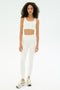 A person with curly hair wears the SPLITS59 Airweight Rib Bra in white, paired with high-waisted white leggings and white sneakers with yellow accents, standing against a plain white background.