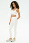 A woman with curly hair models the SPLITS59 Airweight Rib Bra in white, paired with high-waisted white leggings and sneakers, against a plain white background.