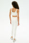 A person with curly hair faces away, wearing the SPLITS59 Airweight Rib Bra in white, paired with high-waisted leggings and white sneakers, against a plain white background.