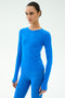 A person stands against a plain background wearing the SPLITS59 Airweight Lite Long Sleeve Waist Length top in Classic Blue, paired with matching blue leggings.