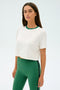 An individual wears the SPLITS59 Djuna Crop Ringer and green leggings against a plain background.