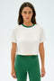 Confidently standing against a plain background, the person sports the stylish SPLITS59 Djuna Crop Ringer in White/Arugula, crafted from a comfortable elastane blend.