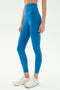 A person stands on a plain white background wearing SPLITS59 Airweight Super High Waist 7/8 leggings in Stone Blue and white athletic shoes, ideal for hot yoga.