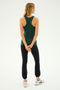 A person with long blonde hair is seen from the back, wearing a green sleeveless top, the Icon High Waist Supplex Legging in black from SPLITS59, and white sneakers, standing with hands clasped behind.