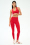 A woman wearing SPLITS59’s Airweight High Waist Legging in Pirate Red with a matching sports bra stands against a white background, pairing the outfit with white sneakers featuring red stripes.