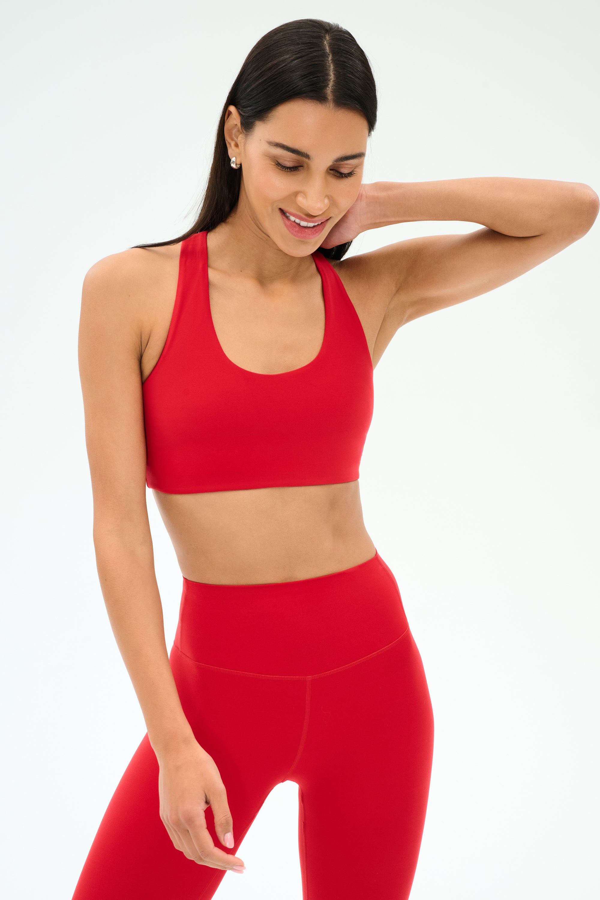 A woman wears the SPLITS59 Sara Airweight Bra in Pirate Red with matching high-waisted leggings, posing against a plain light background—ideal for hot yoga or Pilates.