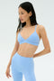 A woman wears the SPLITS59 Theo Rigor Bra in Skylight, paired with matching high-waisted leggings, standing against a plain background.