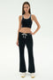 A woman stands facing forward against a plain white background, wearing SPLITS59's Blaire Rib Pant in black paired with a black crop top with white trim and white sneakers.