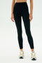 A person wearing SPLITS59 Airweight Rib High Waist 7/8 leggings in black and white sneakers stands against a plain white background.