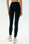 A person stands with their back to the camera against a plain light background, wearing SPLITS59 Airweight Rib High Waist 7/8 leggings in black and white sneakers.