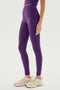 Person standing in SPLITS59 Airweight High Waist Legging in Black Currant, made of an 81% nylon and spandex blend, and beige sneakers on a white background. Photo cropped to show torso to feet.