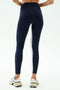A person is seen from the back wearing SPLITS59 Easton Rigor High Waist 7/8 leggings in Indigo/Grass with a white side stripe and white sneakers, standing against a plain background.