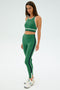 A person is dressed in the Layla Airweight High Waist 7/8 by SPLITS59, featuring arugula with indigo stripes, standing against a plain background and looking at the camera.