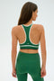 A woman with long brown hair stands against a plain background, her back to the camera, wearing the SPLITS59 Layla Airweight Bra in Arugula/Indigo and matching leggings.