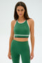 A person wearing a SPLITS59 Layla Airweight Bra in Arugula/Indigo and matching leggings stands against a plain background.