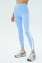 A person is wearing SPLITS59 Miles High Waist Rigor 7/8 leggings in Skylight/White with white athletic shoes, standing against a plain light background.