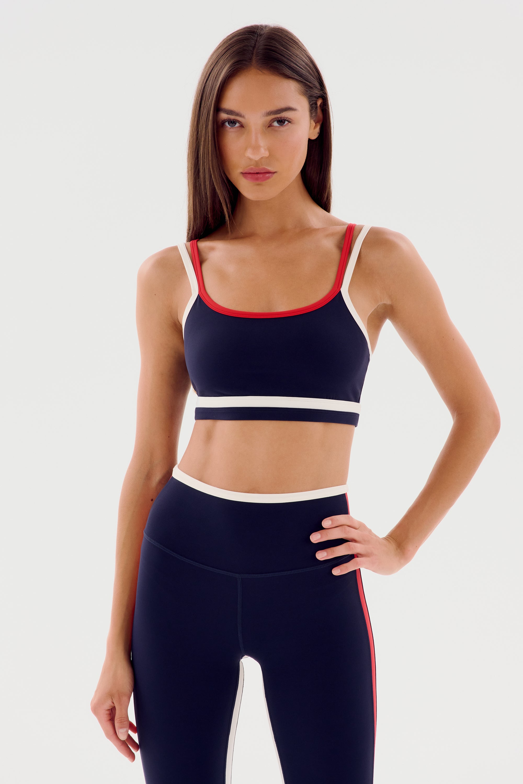 Woman in Eva Rigor Double Strap Bra - Indigo/White by SPLITS59, crafted from a sleek nylon-spandex fabric blend, standing with one hand on her hip.