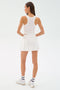 A woman faces away, wearing the SPLITS59 Venus High Waist Rigor Skort in white with a sleeveless top, white socks, and sneakers against a plain light background.