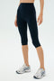 A person wearing SPLITS59 Airweight High Waist 16" Legging in Indigo and white running shoes, standing against a plain light background.