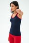 A woman wears the SPLITS59 Ashby Rib Tank in Indigo/Pirate Red with matching leggings, posing against a white background—perfect for yoga or gym sessions.